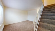 This two-story residence offers a straightforward and functional layout across both levels. The lower level serves as the main entry point, featuring a carpeted open area beneath a staircase with white spindle railings. A closet with visible shelving is conveniently located near the entry door, providing practical storage from the moment you arrive. Textured ceilings are consistent throughout the home, contributing to a classic residential aesthetic.

The upper level hosts the primary living spaces, including a carpeted main living area that connects to additional rooms via a carpeted hallway. A closeted storage space is accessible off the living area. The bedrooms are comfortably sized, each featuring wall-to-wall carpet, baseboard heating, and windows that introduce natural light and views of surrounding greenery. The neutral, cream-toned walls throughout the home create a clean and cohesive backdrop.

The bathroom features a granite-topped vanity with an undermount sink, tile flooring, and baseboard heating, offering a practical and updated finish. The 3D model view reveals an open upper-floor layout with a kitchen counter peninsula, suggesting a connected kitchen and living space. Overall, the home presents a clean, understated design with functional features on each level.