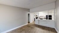 This single-floor unit offers a practical and well-organized layout designed for comfortable everyday living. The open living area is finished with warm wood-tone vinyl flooring and neutral gray walls throughout, creating a cohesive and clean aesthetic. A textured ceiling adds a classic touch, while a half-wall partition with built-in shelving connects the living space to the kitchen, allowing for an open feel while maintaining a defined layout. A walk-in closet is accessible directly from the living area, providing generous storage.

The kitchen is equipped with white cabinetry featuring modern black hardware, dark granite-style countertops, a stainless steel sink, and black appliances including a range and refrigerator. A doorway from the kitchen leads directly into a dedicated laundry room, which houses a full-size washer and dryer.

The two bedrooms each feature the same wood-tone flooring and are fitted with ceiling fans and windows fitted with blinds for natural light and ventilation. A wall-mounted PTAC unit is present in one bedroom. The full bathroom includes a combined tub and shower, a toilet, and a single-sink vanity with white cabinetry, maintaining the clean, updated style found throughout the unit.