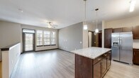 This two-story residence is thoughtfully designed with a consistent aesthetic carried throughout both levels. The main living area adopts an open-concept layout, where the kitchen flows seamlessly into the living room. The kitchen is well-appointed with rich, dark wood cabinetry — including a built-in wine rack — granite countertops, stainless steel appliances, and a central island with pendant lighting overhead. Light wood-style flooring runs throughout the main living spaces, complementing the neutral wall tones and contributing to a clean, modern atmosphere. The living room benefits from a large multi-panel window that draws in natural light and is equipped with a ceiling fan for added comfort. A staircase with a metal handrail connects the two floors, leading to the upper level. Bedrooms are finished with plush carpeting and feature windows that allow ample daylight. The bathrooms are outfitted with granite-topped vanities featuring dark cabinetry, tub-shower combinations with curved curtain rods, and light wood-style tile flooring. A dedicated in-unit laundry area accommodates a full-sized washer and dryer, with an overhead shelf for storage.