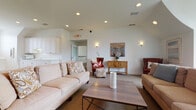 Located at 2828 Marblevista Blvd in Columbus, Ohio, this single-story community clubhouse offers a welcoming and well-appointed gathering space designed for comfort and social engagement. The centerpiece of the facility is a generously sized lounge area featuring vaulted ceilings with recessed lighting and warm wall sconces, creating an inviting ambiance. Plush neutral sofas, accent chairs, and a wood-and-iron coffee table furnish the space, complemented by tasteful wall art and decorative accents.

A secondary seating area provides an additional lounge setup with a wall-mounted flat-screen television, flanked by symmetrical décor and ample natural light filtered through the bright white walls. The space transitions seamlessly into a kitchenette outfitted with full-height white cabinetry, generous countertops, a sink, and a microwave — ideal for hosting events. A separate kitchenette with rich cherry wood cabinetry serves the game room area, which also features billiard cue storage, hinting at recreational amenities nearby.

A bright corridor with carpet flooring, a classic white balustrade, ceiling fan, and statement light fixture connects the various areas, with a windowed entry adding natural light. A quiet reading nook tucked alongside a bookshelf and natural window light completes this versatile, community-focused facility.