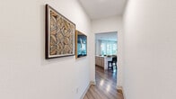 This thoughtfully designed 2-bedroom, 1-bathroom single-floor residence offers a comfortable and contemporary living experience. The open-concept kitchen and living area serves as the heart of the home, featuring light wood cabinetry, white quartz countertops, stainless steel appliances, a tile backsplash, and a kitchen island with bar seating. A full-height pantry cabinet and under-cabinet window allow natural light to brighten the workspace. The living area is anchored by large windows dressed with horizontal blinds and sheer curtains, flooding the space with natural light and offering views of the surrounding neighborhood. Warm hardwood-style flooring runs through the main living areas, while plush carpet adds comfort to the bedrooms. The primary bedroom features a bold teal accent wall, walk-in closet with built-in shelving, and a bright window overlooking greenery. The second bedroom offers a softer sage accent wall with generous natural light. A well-appointed hallway connects the rooms, lined with wall art and leading seamlessly through the layout. The shared bathroom includes a soaking tub with shower, a light wood floating vanity, and clean tile flooring. Two closets provide ample storage throughout the home.