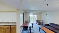 Located at 646 East College Avenue in State College, PA, this 590-square-foot, one-bedroom, one-bathroom apartment offers a functional and practical layout across a single floor. The spacious 240-square-foot bedroom features carpeted floors, a lofted bed frame with built-in storage drawers, a dedicated desk and chair, and a window with vertical blinds that allows natural light in. A wall-mounted HVAC unit provides individual climate control. The bedroom connects directly to a generous walk-in closet equipped with multiple wire shelving units and hanging rods for ample storage. The full bathroom includes a single-sink vanity with wood cabinetry, a large wall mirror, and a tub/shower combination. The kitchen features wood-tone cabinetry, granite-style countertops, hardwood-style flooring, a black electric range, and overhead ventilation. A drop ceiling with a skylight panel brightens the space. The carpeted living room accommodates two dark leather sofas, a coffee table, and additional side tables, creating a comfortable common area. The drop-panel ceilings are consistent throughout the unit, lending a cohesive, understated aesthetic suited for student or young professional living near Penn State University.
