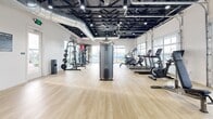 Located at 17645 N Porter Rd in Maricopa, AZ, this single-floor fitness facility offers a generously sized, open-concept layout designed to accommodate a full range of workout activities. The space is divided into a main gym area and a dedicated exercise room, together providing ample room for both cardio and strength training.

The interior features light hardwood-style flooring throughout, which contrasts cleanly against crisp white walls adorned with motivational signage such as "Train Hard" and "Discipline." The exposed black ceiling with visible ductwork and industrial-style track lighting lends the space a modern, energetic aesthetic while maintaining impressive ceiling height.

Large glass panel garage doors — a standout architectural feature — line the perimeter, flooding the gym with abundant natural light and offering open views of the surrounding outdoor amenities, including a pool area. These doors also allow the space to open up entirely, creating an airy, semi-outdoor workout environment.

The gym is outfitted with a comprehensive selection of equipment, including multiple treadmills, ellipticals, stair climbers, cable machines, a Smith machine, free weights, and a punching bag. The exercise room provides additional open floor space, ideal for group classes or functional training. Together, these areas create a bright, welcoming, and fully functional fitness destination.