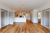Located at 2707 E 6th St in Vancouver, WA, this well-appointed 2-bedroom, 2-bathroom unit offers a thoughtfully designed single-level layout with generous living space. Warm hardwood-style flooring flows throughout the main living areas, complementing the clean, modern aesthetic defined by crisp white walls and gray trim accents.

The open-concept living and kitchen area is bright and welcoming, anchored by a peninsula with pendant lighting overhead and recessed ceiling lights. The kitchen features gray shaker cabinetry, a tile backsplash, stainless steel appliances including a French door refrigerator, and ample counter space. A distinctive arched hallway transitions the space gracefully toward the bedrooms.

The primary bedroom is generously sized, featuring floor-to-ceiling windows and a sliding door that opens to a private balcony with outdoor views. The en-suite primary bathroom includes a dual-sink vanity with gray cabinetry and white countertops, and connects directly to a walk-in closet outfitted with shelving and hanging rods. The second bedroom offers plush carpeting, a roller shade window, and its own wall-mounted climate unit. A dedicated hallway with a second full bathroom completes the layout. A separate walk-in closet provides additional storage throughout the unit.