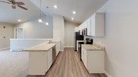 Located in the charming village of Sister Bay, WI, this single-floor residence offers a clean, modern aesthetic with a neutral color palette and consistent finishes throughout. The open-concept kitchen is a standout feature, boasting white shaker-style cabinetry, light granite countertops, stainless steel appliances, and elegant pendant lighting suspended from vaulted ceilings. A peninsula with a built-in sink seamlessly connects the kitchen to the adjoining living area, which is finished with durable wood-look flooring. The bedrooms are carpeted for comfort and warmth, each featuring ceiling fans, closet storage, and baseboard heating. One bedroom includes a convenient walk-in or reach-in closet and offers access to additional hallway space. The unit includes two well-appointed bathrooms: one with a tub-shower combination and the other with a walk-in shower stall. Both bathrooms feature white cabinetry with over-toilet storage, granite-topped vanities, wood-look flooring, and brushed nickel fixtures. Recessed lighting and large mirrors enhance the brightness in these spaces. Overall, the residence presents a cohesive, move-in-ready interior with contemporary finishes suited for comfortable year-round living in Door County.