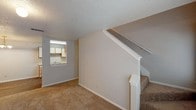 Located at 9811 Copper Creek Dr in Austin, TX, this two-story home offers a well-organized layout designed for comfortable everyday living. The main level features a carpeted living room anchored by a tile-surround fireplace, with a front entry door and windows that bring in natural light. An open pass-through connects the living and dining areas to the galley-style kitchen, which is equipped with white appliances including a range and refrigerator, dual-basin sink, laminate countertops, and a mix of wood and white cabinetry with wood-look vinyl flooring. A separate dining area sits adjacent, illuminated by a chandelier. A staircase with windows at multiple heights draws natural light throughout the vertical transition between floors. Upstairs, multiple carpeted rooms each feature ceiling fans with light fixtures and large windows dressed with vertical blinds, providing ample natural light and outdoor views. Textured ceilings are consistent throughout the home. The layout flows logically between spaces, and the neutral color palette throughout creates a clean, versatile backdrop well-suited for a variety of interior styles.