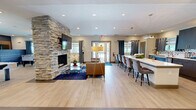 Located at 3544 Saint Johns Bluff Rd S in Jacksonville, Florida, this thoughtfully designed single-floor community space offers a welcoming and multifunctional environment ideal for socializing and collaboration. The interior is defined by light wood-look flooring, crisp white ceilings with recessed lighting, and a bold navy blue accent wall that creates visual depth throughout.

The foyer sets the tone with an elegant console table, decorative mirror, and a statement chandelier, leading seamlessly into the main living area. A dramatic stacked stone column anchors the room, housing a fireplace and wall-mounted television, surrounded by comfortable lounge seating on a deep blue area rug. The space also accommodates a ping pong table and foosball table, making it a versatile recreation hub.

The fully equipped kitchen features dark espresso cabinetry, quartz countertops, a mosaic tile backsplash, stainless steel appliances, and a large island with bar seating — all illuminated by modern pendant lighting. Adjacent areas include a computer workstation lounge and a glass-enclosed private meeting room, ensuring the space serves both leisure and productivity needs. Natural light filters in through multiple windows dressed with layered roller shades and navy curtains, enhancing the space's modern, polished ambiance.