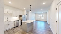 Located at 1200 S 44th St in Rogers, Arkansas, this single-story home offers a thoughtfully designed layout with three bedrooms, three bathrooms, and a dedicated laundry room. The interior features a consistent, modern aesthetic highlighted by light wood-tone luxury vinyl plank flooring, crisp white walls, and recessed lighting throughout.

The open-concept kitchen and living area form the heart of the home. The kitchen is well-appointed with white shaker-style cabinetry, black hardware accents, light quartz countertops, stainless steel appliances including a refrigerator, dishwasher, range, and microwave, and a central island with pendant lighting. The living area flows seamlessly from the kitchen, receiving natural light through large windows and a glass-panel exterior door.

Each bedroom is equipped with a ceiling fan and generously sized windows that bring in natural light and outdoor views. The primary bedroom connects directly to a private en-suite bathroom featuring a long white vanity with dual sinks and a walk-in closet with built-in shelving and hanging rods.

The bathrooms maintain a clean, contemporary look with white wave-textured walk-in showers, white cabinetry, and wood-look flooring. The dedicated laundry room includes a full-size washer and dryer, upper cabinetry, and additional counter space, providing practical everyday convenience.