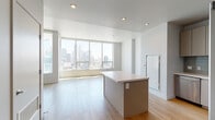 Located in the heart of Downtown Los Angeles, this modern high-rise unit at 1133 S Hope St offers a sleek, contemporary living experience defined by clean lines, light-toned hardwood flooring, and an abundance of natural light throughout. The open-concept living and dining area is anchored by expansive floor-to-ceiling windows that frame striking panoramic views of the Los Angeles skyline, flooding the space with daylight and creating a seamless connection to the city below.

The kitchen is well-appointed with stainless steel appliances — including a gas range, over-the-range microwave, and French door refrigerator — complemented by taupe flat-front cabinetry, a subway tile backsplash, and a central island with a white quartz countertop ideal for both meal preparation and casual dining.

The bedrooms are generously proportioned, each featuring light hardwood floors, neutral walls, and large windows that invite natural light and offer additional city views. The unit includes two bathrooms: a primary bath with a frameless glass walk-in shower and large-format tile, and a secondary bath featuring a soaking tub with a sliding glass enclosure, modern vanity, and tile flooring. The overall aesthetic is clean, minimalist, and well-suited to contemporary urban living.