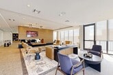 Located at 101 SW 1st St in Dania Beach, Florida, this expansive amenity lounge offers a sophisticated, contemporary design across a generously proportioned single floor. The space is defined by its open-plan layout, soaring ceilings, and floor-to-ceiling windows that flood the interior with natural light and frame bright Florida skies. A distinctive slatted wood accent wall serves as a striking architectural focal point, complementing the warm, neutral tones found throughout.

The lounge is divided into several well-appointed zones. Multiple seating areas are furnished with an eclectic yet cohesive mix of leather wingback chairs, rounded accent chairs, plush sofas, and sleek side tables, all anchored by abstract area rugs atop polished terrazzo-style flooring. A central reception or social desk with channel-tufted wood paneling adds a refined, hospitality-inspired element.

A game and entertainment area features a billiards table beneath a sculptural pendant light, alongside a stylish wet bar with navy fluted cabinetry, pendant lighting, and built-in shelving. Curated artwork and decorative accessories are displayed throughout, enhancing the upscale ambiance.

An adjacent balcony extends the space outdoors, offering additional space to enjoy the South Florida climate. The overall design is modern, warm, and inviting — ideal for socializing or relaxing.