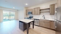 This thoughtfully designed one-bedroom, one-bathroom unit in Bloomington, MN offers a smart and functional layout across a single floor. The open kitchen is a standout feature, showcasing taupe shaker-style cabinetry, stainless steel appliances including a range, microwave, dishwasher, and refrigerator, crisp white countertops, a subway tile backsplash, a matte black faucet, and a movable island that adds both prep space and versatility. Light wood-tone flooring runs throughout the main living and kitchen areas, lending a clean, contemporary feel. The bedroom is a comfortable retreat finished with plush carpet, warm neutral walls, and a tray ceiling that adds architectural interest. A large window floods the room with natural light and provides views of the surrounding exterior. A dedicated walk-in closet with built-in shelving and rod space offers generous storage. The bathroom features light wood-look flooring, a wood-toned vanity with matte black hardware, and a clean, minimal aesthetic. Throughout the unit, shaker-panel doors with matte black hardware provide a cohesive modern touch. This well-appointed unit is ideal for those seeking a low-maintenance, contemporary living space in a convenient Bloomington location.