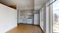 This single-floor residence combines contemporary design with thoughtful finishes throughout. The kitchen serves as a central highlight, outfitted with sleek flat-front cabinetry in a soft grey tone, gold-accented hardware, a striking marble-style backsplash, and white appliances including a gas range, built-in microwave, dishwasher, and full-size refrigerator. A gold faucet over a clean white countertop sink adds an elegant touch, while warm hardwood floors in a wide-plank format extend seamlessly through the living areas, tying the space together.

The living area benefits from oversized windows that frame urban cityscape views, allowing generous natural light to fill the room and create an open, airy atmosphere. A separate room features a bold, artistic wall covering with sweeping tones of terracotta and slate, giving the space a distinctive and creative character.

The bathroom maintains a clean, classic aesthetic with white square subway tile walls, dark slate-toned floor tiles, and gold towel bar and paper holder accents that echo the brass detailing found throughout the residence. A hallway connects the rooms efficiently, with a thermostat conveniently positioned near the kitchen entry. This well-appointed space delivers a cohesive blend of modern urban style and refined detail.