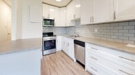 Located at 3 Slessor Blvd in Grimsby, Ontario, this efficiently designed single-floor unit offers a well-planned layout comprising a living room, kitchen, and full bathroom. The living room features light-toned laminate flooring, crisp white walls, and a door with an adjacent window that frames views of lush greenery outside, allowing natural light to fill the space. Baseboard heating runs along the perimeter, ensuring year-round comfort. The kitchen is a standout feature, finished with bright white shaker-style cabinetry, light grey subway tile backsplash, and neutral quartz-tone countertops. A full suite of stainless steel appliances — including a refrigerator, electric range with over-the-range microwave, and dishwasher — provides modern functionality. Large windows bring in ample natural light, enhancing the clean, airy feel of the space. Light hardwood-style flooring ties the kitchen seamlessly to the rest of the unit. The bathroom is neatly appointed with beige floor tiles, white vertical subway tile surrounding a full soaker tub and shower, and brushed nickel fixtures and towel bars, delivering a clean and timeless finish throughout.