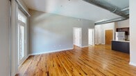 Located at 3400 Stratford Rd NE in Atlanta's Buckhead neighborhood, this 2-bedroom, 2-bathroom residence offers an industrial-chic aesthetic defined by warm hardwood floors, high ceilings, and signature exposed metallic ductwork running throughout the open living areas. The combined living, dining, and kitchen space forms a generous open-concept layout, flooded with natural light from large French doors that open to an outdoor balcony area with views of the surrounding greenery. The kitchen is well-appointed with rich dark-wood cabinetry, granite countertops, a central island, tile backsplash, and a full suite of stainless steel appliances, including a refrigerator, range, and microwave. Track lighting illuminates the space with a modern touch. The primary bedroom is spacious, featuring hardwood flooring and a ceiling fan, while the ensuite bathroom offers tile flooring, a glass-enclosed shower, and white cabinetry with granite counters. The second bathroom mirrors this refined finish with a granite vanity and tile floors. Both bedrooms benefit from natural light via large windows. Four closets and a dedicated utility room provide ample storage throughout. The unit's loft-inspired character and polished finishes create a cohesive blend of urban style and residential comfort.