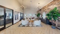 Located at 1030 S Dobson Rd in Mesa, Arizona, this thoughtfully designed living room makes a strong architectural impression from the moment you enter. The space is anchored by striking herringbone-patterned tile flooring in a warm, light wood tone that adds visual depth and sophistication throughout. Soaring vaulted ceilings clad in whitewashed wood planking lend an airy, open feel, while two elegant wrought-iron chandeliers provide both ambient light and a refined decorative focal point.

A full-height reclaimed wood accent wall serves as the room's dramatic centerpiece, offering rich texture and a rustic-modern contrast against the crisp white walls. Large black-framed glass doors and windows on multiple sides flood the space with natural light and offer views of the surrounding outdoor greenery, creating a seamless indoor-outdoor connection.

The living area is furnished with plush, curved white lounge chairs arranged around a natural wood coffee table atop a geometric diamond-patterned area rug, providing a comfortable and inviting gathering space. A dark console unit with an arched mirror and decorative accessories anchors one side of the accent wall, while a lush fiddle-leaf fig tree adds a vibrant natural element. Abstract wall art and a neutral bench complete the well-curated, contemporary aesthetic of this welcoming space.