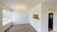 This single-floor, 3-bedroom, 2-bathroom residence offers a practical and comfortable layout designed for everyday living. The main living and dining areas feature durable wood-look flooring throughout, with a textured ceiling and a pendant light fixture that anchors the dining space. A pass-through window with a built-in shelf connects the dining area to the kitchen, creating an open and communicative flow between rooms.

The galley-style kitchen is efficiently designed with white cabinetry trimmed in warm wood tones, dark countertops, and black appliances including a refrigerator and electric range. Ample cabinetry provides generous storage, and the layout maximizes workspace along both walls.

The living area benefits from multiple windows that invite natural light and provide outdoor views, creating a bright and welcoming atmosphere. The three bedrooms are carpeted for comfort, each featuring neutral tones and windows that bring in natural light — one notably featuring a large picture window with exterior views.

Both bathrooms are finished with clean, white surrounds, tub-shower combinations with brushed nickel fixtures, and vanities with dark countertops. The overall aesthetic of the residence is clean and neutral, offering a versatile canvas well-suited to a variety of living arrangements.