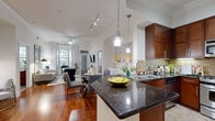 Located at 3443 Kingsboro Rd NE in Atlanta's prestigious Buckhead neighborhood, this well-appointed single-floor residence offers a refined living experience defined by quality finishes and a thoughtfully designed open-concept layout. The kitchen serves as a central highlight, showcasing rich dark wood cabinetry, polished dark granite countertops with a breakfast bar overhang, a stone tile backsplash, stainless steel appliances including a gas range and built-in microwave, and elegant pendant lighting overhead. The kitchen flows seamlessly into the dining and living areas, all unified by warm hardwood flooring and crown molding throughout. The living room is bright and airy, featuring tall windows dressed with floor-to-ceiling curtains that invite generous natural light and views of surrounding greenery. The primary bedroom offers a tranquil retreat with plush carpeting, large windows, and access to a spacious en-suite bathroom complete with dual vanities, a soaking tub, a separate glass-enclosed shower, and large-format tile flooring. A generous walk-in closet provides ample storage. An additional walk-in closet with laundry facilities adds further convenience. Crown molding and track lighting are consistent design elements that contribute to the polished, cohesive ambiance throughout the residence.
