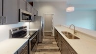 This single-floor residence offers a thoughtfully designed layout with a cohesive neutral color palette throughout. The living area is highlighted by wide-plank hardwood-style flooring, a ceiling-mounted light fixture, and a large sliding glass door that opens to a private balcony, allowing natural light to fill the space and providing views of the surrounding building exterior.

The galley-style kitchen is well-equipped with gray cabinetry, stainless steel appliances including a built-in microwave, electric range, and refrigerator, complemented by light quartz countertops and a double-basin undermount sink. A pendant light adds a finishing touch. An adjacent alcove houses a stacked washer and dryer for in-unit laundry convenience.

The bedrooms feature plush wall-to-wall carpeting, neutral taupe walls, and ceiling fans. One bedroom includes a walk-in closet with built-in hanging rods. A utility closet with an accessible electrical panel and shelving provides added storage.

Both bathrooms are finished with large-format tile flooring and quartz-topped white vanities. The primary bathroom features a soaking tub with tiled surround and rain showerhead, while the secondary bathroom offers a glass-enclosed walk-in shower with chrome fixtures.