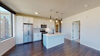 Located at 609 S Cascade Ave in Colorado Springs, Colorado, this modern single-floor residence showcases a thoughtfully designed open-concept layout with high-end finishes throughout. The kitchen is a standout feature, boasting crisp white shaker cabinetry, a herringbone-patterned tile backsplash, stainless steel appliances, and a central island with an integrated sink and elegant pendant lighting overhead. Rich, dark hardwood flooring flows seamlessly through the main living and kitchen areas, creating a warm yet contemporary aesthetic. Large floor-to-ceiling windows flood the living space with natural light and frame sweeping views of the Colorado mountains and the surrounding cityscape, with access to a private balcony. The bedroom is carpeted for comfort and includes a walk-in closet, providing generous storage. The bathroom is finished with large-format marble-look wall tiles surrounding the soaking tub and shower, complemented by matte black fixtures and neutral floor tiling that tie the modern design together. Clean lines, a neutral color palette, and quality materials define the overall ambiance of this well-appointed Colorado Springs residence.