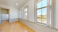 This single-floor space combines classic architectural details with modern finishes to create a clean, functional living environment. The kitchen is a standout feature, offering dark espresso cabinetry extending to the ceiling, light stone-look countertops, and a full suite of black appliances including a refrigerator, electric range, and dishwasher, all set atop warm hardwood flooring that flows throughout the unit.

The individual rooms are bright and minimalist, characterized by crisp white walls, light hardwood floors, and windows framed with traditional millwork. Several rooms feature charming beadboard wainscoting that adds texture and architectural character. A dedicated closet space equipped with a wire hanging rod provides practical storage.

A sun-filled room with vaulted ceilings and a row of large double-hung windows offers expansive outdoor views of surrounding greenery, filling the space with abundant natural light throughout the day. The bathrooms are finished in a contemporary style, featuring light tile flooring, a full vanity with dark wood cabinetry and a white countertop, a large mirror with overhead lighting, and grab bars for accessibility. The overall ambiance of the space is bright, airy, and move-in ready, with a thoughtful blend of traditional detailing and modern utility.