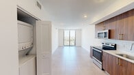 Located at 218 NW Eighth St in Miami, FL, this modern high-rise unit offers a bright, open-concept layout finished with large-format porcelain tile flooring throughout. The living and dining area flows seamlessly toward floor-to-ceiling sliding glass doors that open onto a private balcony, framing sweeping panoramic views of the Miami skyline and surrounding cityscape. A ceiling fan adds comfort to this light-filled space.

The kitchen is outfitted with rich walnut-toned cabinetry accented by gold hardware, white quartz countertops, a classic subway tile backsplash, and a full suite of stainless steel appliances including a French door refrigerator, electric range, built-in microwave, and dishwasher. An in-unit stacked washer and dryer is conveniently housed behind a dedicated closet panel.

The bedrooms are generously proportioned, with clean white walls, tile flooring, and ample closet storage. Both bathrooms reflect a refined aesthetic, featuring walnut vanities with quartz countertops, gold-accented fixtures, large mirrors, and fully tiled tub-shower combinations with striking marble-look wall tile. The unit's crisp, neutral palette and contemporary design details create a cohesive and polished living environment throughout.