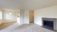 This single-floor space is thoughtfully laid out to maximize functionality and comfort. The living area serves as the heart of the home, featuring a brick-surround fireplace that adds a classic, cozy focal point to the room. Neutral-toned carpet flows throughout the living and bedroom areas, contributing to a warm and cohesive atmosphere. A textured popcorn ceiling is consistent throughout the space.

The kitchen is efficiently designed in a U-shaped configuration, offering ample white cabinetry with contrasting trim for storage, light-toned countertops, a double stainless steel sink, and white appliances including an electric range and dishwasher. Light hardwood-style flooring in the kitchen provides a practical contrast to the carpeted areas. A pass-through connects the kitchen to the living area, enhancing the open feel of the space.

The bedrooms are generously sized, each featuring plush carpet, white walls, and windows fitted with blinds that allow natural light while maintaining privacy. Baseboard heaters in each bedroom ensure consistent warmth. One area of the space opens to a private balcony through a sliding glass door, offering outdoor views of the surrounding neighborhood. The bathroom includes a standard tub and shower combination with clean, neutral finishes.
