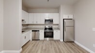 Located at 66 Hawthorne Dr in Bedford, NH, this single-floor residence offers two bedrooms and two full bathrooms in a well-organized layout. The kitchen is a standout feature, outfitted with crisp white shaker-style cabinetry, granite countertops, a full suite of stainless steel appliances including a range, microwave, dishwasher, and refrigerator, and light hardwood-style flooring that extends into the main living area. The open entry area provides a clean, neutral backdrop with a modern door entry and thermostat panel.

Both bedrooms are carpeted in a warm neutral tone and feature natural light through double-hung windows with views of surrounding trees. The spacious primary bedroom offers ample room and is well-proportioned for comfortable living. The second bedroom also includes a closet and window, providing a bright, versatile space.

The two bathrooms are finished with large-format tile flooring and granite-topped vanities with white cabinetry. One bathroom features an accessible walk-in shower with brushed nickel grab bars, while the second bathroom provides a similarly clean, functional design. Neutral warm-gray walls throughout the entire residence create a cohesive and modern aesthetic suited to a variety of furnishing styles.