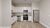 Located at 66 Hawthorne Dr in Bedford, NH, this single-floor residence offers two bedrooms and two full bathrooms in a well-organized layout. The kitchen is a standout feature, outfitted with crisp white shaker-style cabinetry, granite countertops, a full suite of stainless steel appliances including a range, microwave, dishwasher, and refrigerator, and light hardwood-style flooring that extends into the main living area. The open entry area provides a clean, neutral backdrop with a modern door entry and thermostat panel.

Both bedrooms are carpeted in a warm neutral tone and feature natural light through double-hung windows with views of surrounding trees. The spacious primary bedroom offers ample room and is well-proportioned for comfortable living. The second bedroom also includes a closet and window, providing a bright, versatile space.

The two bathrooms are finished with large-format tile flooring and granite-topped vanities with white cabinetry. One bathroom features an accessible walk-in shower with brushed nickel grab bars, while the second bathroom provides a similarly clean, functional design. Neutral warm-gray walls throughout the entire residence create a cohesive and modern aesthetic suited to a variety of furnishing styles.