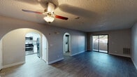 This single-floor residence offers a well-organized layout with a blend of practical design and comfortable living spaces. The open living area serves as the heart of the home, featuring durable wood-style flooring, a ceiling fan with light fixture, and a textured ceiling. Distinctive arched doorways frame transitions to the kitchen and a laundry area, adding a classic architectural touch. A sliding glass door fills the living space with natural light and provides direct access to an outdoor patio area with views of surrounding greenery.

The kitchen is equipped with white cabinetry, speckled granite-style countertops, a double stainless steel sink, and a window that brings in additional natural light. Appliances including a refrigerator and range are included.

The bedrooms are carpeted for comfort, with one featuring a walk-in closet and a window that allows natural light to filter in. The second bedroom includes a closet with shelving and its own window.

Two bathrooms serve the residence. One includes a vanity with speckled countertop, a large mirror, and a glass-enclosed shower. The second bathroom features a matching vanity and a bathtub-shower combination with a curved curtain rod. Both bathrooms are finished with wood-style flooring. A dedicated laundry area is conveniently accessible from the main living space.