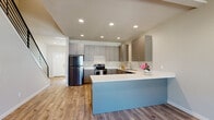 This well-designed 3-floor home offers a thoughtful layout suited for multi-generational living or flexible use across its levels. The main floor showcases a contemporary open-concept kitchen featuring sleek grey cabinetry, white countertops, stainless steel appliances, and a striking powder-blue peninsula that anchors the space. Warm wood-look flooring and recessed lighting create a bright, welcoming atmosphere throughout. A clean, neutral-toned bathroom with a white vanity countertop and tile flooring serves this level, with a window providing natural light. A secondary kitchen on another floor mirrors the modern aesthetic, equipped with grey cabinetry, white countertops, a stainless dishwasher, and an electric range — complete with its own wood-look flooring. An additional open room on this floor includes a wall-mounted mini-split unit and access to a private entrance, offering versatile functionality. The bathrooms throughout the home are consistently finished with grey vanities, chrome fixtures, and tile flooring. The lower level features an unfinished room with carpet ready for installation, presenting an opportunity for customization. An attached two-car garage with a standard overhead door completes the home, adding practical storage and parking convenience.