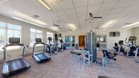 Located at 535 Blackrock Dr in Blacksburg, Virginia, this fitness center is a well-appointed, single-floor facility designed to support a comprehensive workout experience. The space is thoughtfully organized into distinct exercise zones, each serving a specific training purpose.

The cardio area is generously equipped with multiple treadmills, elliptical trainers, and a stationary bike, all positioned near large windows that invite abundant natural light and offer pleasant outdoor views of the surrounding landscape. Ceiling fans help maintain a comfortable environment throughout the space.

A dedicated strength training zone houses a multi-station cable machine along with benches and additional resistance equipment, providing ample options for full-body strength workouts. Adjacent to this is a free weights area stocked with a comprehensive dumbbell rack and multiple medicine ball stands, catering to both traditional and functional training styles.

The facility features a drop ceiling with recessed panel lighting that evenly illuminates the entire floor, while patterned carpet tiles provide a durable yet comfortable underfoot surface. Mirrored wall panels near the strength equipment enhance the sense of space and allow users to monitor their form. The layout is open and well-organized, ensuring ease of movement between exercise stations. Overall, the fitness center offers a clean, functional, and inviting environment for residents and users seeking a well-rounded training facility.