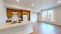 Located at 2065 South River Parkway in Portland, Oregon, Unit 601 is a well-appointed single-floor residence offering a thoughtfully designed open layout with modern finishes throughout. The open-concept kitchen and living area serves as the heart of the unit, featuring a central island with a light stone countertop, warm-toned wood cabinetry, recessed lighting, and white appliances including a refrigerator and electric range. Durable hardwood-style flooring flows through the main living areas, creating a cohesive and inviting atmosphere. The spacious living area receives natural light through large windows that frame views of the surrounding Portland cityscape. The bedrooms are carpeted for comfort and each features generous windows that allow abundant natural light and outdoor views of the city and surrounding hills. Two bathrooms serve the unit — a full bathroom complete with a soaking tub, shower, and wood-accented vanity, and a second half or three-quarter bath with a matching vanity and tile flooring. Additional features include a utility panel, ample storage with open shelving visible near the kitchen, and ceiling fans in the bedrooms. The unit presents a clean, contemporary aesthetic with neutral tones and practical finishes throughout.
