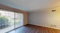 Located at 1535 Woods Rd in Winston-Salem, NC, this single-floor unit offers a thoughtfully designed layout with consistent finishes throughout. The living area is a standout space, showcasing rich wood-look hardwood flooring, crown molding, and neutral gray walls that create a clean, modern aesthetic. A large sliding glass door fitted with vertical blinds floods the room with natural light while providing direct views of the surrounding greenery outdoors.

The entryway features the same durable wood-look flooring, crown molding, and a small pass-through window that connects to an adjacent area, adding a functional architectural detail. Two interior doors provide access to additional spaces from this entry point.

The galley-style kitchen is well-appointed with white cabinetry, granite-look countertops, a stainless sink, and black appliances including a refrigerator, range, and dishwasher. Recessed lighting and wood-look flooring complete the space efficiently.

The bedrooms are carpeted in a neutral gray tone and feature crown molding and windows that allow natural light. The bathroom includes a full tub and shower combination with white tile surround and chrome fixtures, complemented by gray walls for a clean finish throughout.