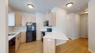 This well-appointed single-floor residence offers a clean, modern aesthetic with a thoughtfully designed layout visible across all its living spaces. Light hardwood-style flooring flows consistently throughout, creating a cohesive and warm atmosphere from room to room.

The kitchen is a standout feature, showcasing light wood cabinetry with matte black hardware, crisp white countertops, and a full suite of black appliances including a refrigerator, electric range, and over-the-range microwave. A peninsula with a breakfast bar overhang provides additional counter space and a casual dining option, opening conveniently to the adjacent living and dining area.

The combined living and dining space is bright and airy, with multiple windows fitted with horizontal blinds that allow natural light to filter in. An elegant chandelier and a ceiling fan with a light kit add both style and functionality to this central gathering area.

The bedrooms are comfortably sized, each featuring hardwood-style flooring, neutral walls, and windows that bring in natural light. Closet space is readily available in each room.

The bathrooms are notable for their decorative patterned tile flooring, which adds a stylish touch. Each bathroom includes a light wood vanity with a white countertop, a mirror, and a tub-shower combination. Built-in storage cabinetry provides added convenience. The overall design is clean, contemporary, and move-in ready.