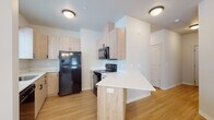 This well-appointed single-floor residence offers a clean, modern aesthetic with a thoughtfully designed layout visible across all its living spaces. Light hardwood-style flooring flows consistently throughout, creating a cohesive and warm atmosphere from room to room.

The kitchen is a standout feature, showcasing light wood cabinetry with matte black hardware, crisp white countertops, and a full suite of black appliances including a refrigerator, electric range, and over-the-range microwave. A peninsula with a breakfast bar overhang provides additional counter space and a casual dining option, opening conveniently to the adjacent living and dining area.

The combined living and dining space is bright and airy, with multiple windows fitted with horizontal blinds that allow natural light to filter in. An elegant chandelier and a ceiling fan with a light kit add both style and functionality to this central gathering area.

The bedrooms are comfortably sized, each featuring hardwood-style flooring, neutral walls, and windows that bring in natural light. Closet space is readily available in each room.

The bathrooms are notable for their decorative patterned tile flooring, which adds a stylish touch. Each bathroom includes a light wood vanity with a white countertop, a mirror, and a tub-shower combination. Built-in storage cabinetry provides added convenience. The overall design is clean, contemporary, and move-in ready.