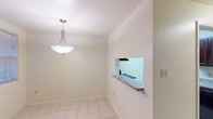 This single-floor, 1-bedroom, 1-bathroom unit offers a practical and well-organized layout. The kitchen is designed in a galley style, featuring dark espresso cabinetry paired with granite-look countertops, tile flooring, and black appliances including a range, overhead microwave, and refrigerator. A pass-through window with a granite-look ledge connects the kitchen to the adjacent dining area, enhancing the sense of openness between the two spaces.

The dining area is a defined space highlighted by a stylish pendant light fixture and light tile flooring. A notable architectural detail is the painted white brick wall, which adds texture and character to both the dining area and the bedroom. Natural light enters through windows fitted with blinds in both rooms.

The bedroom is a comfortable retreat featuring carpet flooring, a ceiling fan with a light kit, a window for natural light, and access to a closet. The painted brick wall continues here, lending a consistent design element throughout the unit.

The bathroom is clean and straightforward, outfitted with a tub-shower combination, a toilet, a vanity with a sink, and a dark-framed mirror. Light tile flooring ties the wet areas of the unit together cohesively, creating a unified and functional living space.