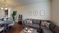 This three-story townhome offers a thoughtfully designed layout that balances functional living spaces with a clean, modern aesthetic. The kitchen is a standout feature, outfitted with dark espresso cabinetry, light quartz countertops, subway tile backsplash, and stainless steel appliances, including a refrigerator, range, microwave, and dishwasher. A pantry provides additional storage, and rich hardwood-style flooring extends throughout the main level.

The living area is generously sized with room for a large sectional sofa and features a ceiling fan, a window inviting natural light, and warm neutral walls that create a relaxed atmosphere. A convenient half bath with a pedestal sink and oval mirror is also located on the main floor.

Upper levels include well-proportioned bedrooms with plush carpeting. The primary bedroom accommodates a king-size bed and includes a ceiling fan. Additional bedrooms offer versatility, with one configured as a home office featuring a window with natural light. Bedrooms include closets with sliding doors and ample storage space. Connecting hallways are bright and open, contributing to the home's overall sense of flow and accessibility across all three floors.