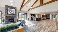 Located at 265 Bear Christiana Rd in Bear, Delaware, this single-floor community amenity space offers a generously sized and thoughtfully designed environment for both relaxation and activity. The welcoming lounge area immediately impresses with soaring vaulted ceilings accented by warm wood beams, a striking stacked-stone fireplace, and expansive floor-to-ceiling windows that flood the space with natural light. Light wood-look flooring and tasteful furnishings carry throughout, creating a cohesive and contemporary aesthetic. An adjacent kitchen bar and dining area, complete with mosaic tile accents and pendant lighting, provide a social hub ideal for gatherings. The game room features a pool table, shuffleboard, and a mounted TV, all set against bold green and slate accent walls with vaulted ceilings and large windows offering outdoor views. A dedicated lounge alcove with a sectional sofa and high-top seating adds to the communal atmosphere. The fitness facilities are comprehensive, encompassing a cardio room equipped with treadmills, ellipticals, and a rowing machine, as well as a separate free weights and strength training room with mirrored walls and rubber flooring. Together, these amenities deliver a well-rounded, resort-style community experience.