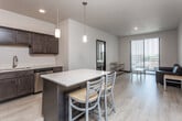 This well-appointed single-floor residence offers a thoughtfully designed open-concept layout that seamlessly connects the kitchen, dining, and living areas. The kitchen is a standout feature, outfitted with rich dark-stained cabinetry, light quartz countertops, a full suite of stainless steel appliances including a French door refrigerator, range, microwave, and dishwasher, and a central island with seating for two — illuminated by sleek pendant lighting. The living area benefits from natural light streaming through a sliding glass door that opens to a balcony with urban views. Two bedrooms offer quiet retreats, each with large windows fitted with horizontal blinds, light hardwood-style flooring, and ample space for furnishings. The unit includes two full bathrooms, each featuring a tub/shower combination, vanity with dark cabinetry and a white countertop, and framed mirrors. A dedicated in-unit laundry room houses a full-size top-loading washer and dryer with wire shelving for added storage. Throughout the space, light hardwood-style flooring, neutral wall tones, and recessed lighting create a clean, contemporary aesthetic well-suited for everyday living.