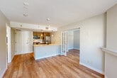 This 2-bedroom, 2-bathroom residence in Tewksbury, MA offers a well-designed, single-floor layout that makes efficient use of its space. The open-concept living area flows seamlessly from the kitchen through the dining space and into the living room, creating a bright and cohesive environment. Large windows throughout allow natural light to fill the rooms while framing pleasant views of surrounding foliage.

The kitchen is a functional centerpiece, featuring a peninsula with a white quartz countertop, an undermount sink with a matte black faucet, warm wood cabinetry, and a full suite of stainless steel appliances including a refrigerator, range, and microwave. Pendant lighting above the peninsula adds a modern touch.

The bedrooms are comfortably sized, with the primary bedroom offering built-in closet space. Both rooms feature the same hardwood-style flooring found throughout the unit, neutral wall tones, and windows with views of the tree canopy outside.

The two bathrooms are clean and functional. One features a rich red wood vanity with a granite countertop and a framed mirror, while the other includes a full soaking tub with a shower. Both baths are finished with tile flooring. French doors and a textured ceiling in select areas add subtle architectural character throughout this well-appointed residence.