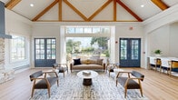 Located at 1520 N Beckley Ave in Dallas, TX, this single-floor space offers a thoughtfully designed interior that blends modern elegance with warm, rustic character. The living room is an architectural showpiece, boasting soaring vaulted ceilings with exposed wood beam trusses and light hardwood flooring throughout. A striking stone fireplace with a slate-blue surround serves as the focal point of the living area, complemented by large French doors and expansive floor-to-ceiling glass panels that flood the space with natural light and offer views of an outdoor pool area. The kitchen is equally impressive, featuring navy-blue cabinetry with brass hardware, a crisp white countertop, and a vibrant teal subway tile backsplash. A floor-to-ceiling slatted wood accent wall adds warmth and texture, while pendant lighting illuminates a generous white island with bar seating. Stainless steel appliances, including a full-size French door refrigerator, complete the functional layout. A connecting hallway provides access between areas, maintaining the open and airy flow of the space. Interior French doors with grid-pane glazing add a refined architectural detail, further enhancing the bright, welcoming ambiance throughout this well-appointed Dallas property.