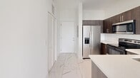 Located at 1 Curtiss Pkwy in Miami Springs, Florida, this thoughtfully designed one-bedroom, four-bathroom residence offers a clean, contemporary aesthetic throughout its well-utilized single floor. Polished marble-look porcelain tile flows seamlessly across every room, lending a bright, upscale feel to the entire space.

The open-concept kitchen and living area serves as the heart of the home. The kitchen is outfitted with rich dark-wood cabinetry, sleek quartz countertops, and a full suite of stainless steel appliances, including a French-door refrigerator, electric range, built-in microwave, and dishwasher. A peninsula with an undermount sink provides additional prep space and connects the kitchen to the airy living area, which is bathed in natural light from large, black-framed windows offering views of lush tropical greenery.

The primary bedroom is generously proportioned, featuring the same polished tile flooring, crisp white walls, and a large window with palm tree views, reinforcing the South Florida atmosphere. Two closets provide practical storage throughout the unit.

The four bathrooms are finished in a consistent modern style, featuring marble-look tile, quartz vanity tops, undermount sinks, large mirrors, and brushed gold or chrome fixtures. A hallway connects all areas efficiently, with a welcoming entry foyer completing the layout.
