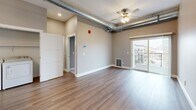 Located at The Elements in Rapid City, South Dakota, this thoughtfully designed single-floor unit blends modern finishes with industrial character. The open living area showcases warm hardwood-style flooring, neutral tones, and exposed ductwork that adds an urban loft aesthetic. A ceiling fan and sliding glass door lead to a private balcony overlooking the surrounding cityscape, allowing natural light to fill the space.

The kitchen is a standout feature, outfitted with crisp white shaker cabinetry, sleek black hardware, a striking marble-style quartz island and countertops, and a full suite of stainless steel appliances including a refrigerator, range, microwave, and dishwasher. A pendant light above the island adds a refined finishing touch.

The bedrooms are carpeted for comfort, each offering ample natural light through well-placed windows with views of the neighboring architecture. Generous closet space is provided, including a walk-in closet. The bathroom is clean and functional, featuring a white vanity with dual sinks, hardwood-style flooring, and a full tub-shower combination. Additional storage and a dedicated laundry area round out the practical layout of this well-appointed urban residence.