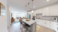 Located at 2705 Haverford Pl in Charlotte, NC, this one-bedroom, one-bathroom residence offers a thoughtfully designed open-concept floor plan. The kitchen serves as a central highlight, featuring crisp white shaker cabinetry, granite countertops, a subway tile backsplash, and a full suite of stainless steel appliances including a refrigerator, range, microwave, and dishwasher. A kitchen island with seating provides additional counter space and a casual dining option, while pendant lighting adds a modern touch overhead.

The kitchen flows seamlessly into the living and dining area, where large windows allow abundant natural light to fill the space. Light wood-tone flooring runs throughout the main living areas, complementing the clean, neutral color palette. A dedicated dining nook near the windows offers a bright, airy spot for meals.

The bedroom is carpeted for comfort and features a large window with views of surrounding greenery, a ceiling fan, and direct access to a walk-in closet. The bathroom is well-appointed with a granite-topped vanity, gray cabinetry, a tub-shower combination with tile surround, and wood-look flooring. A hallway connects the rooms efficiently, completing this well-organized and stylish Charlotte residence.