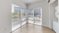 Located at 120 20th Ave S in Nashville, Tennessee, this efficient single-floor unit offers a well-designed layout that maximizes every square foot. The open living area is anchored by large corner windows fitted with horizontal blinds, flooding the space with natural light while framing views of the surrounding Nashville cityscape and greenery.

The kitchen is a standout feature, outfitted with modern gray cabinetry — both upper and lower — granite-style countertops, a stainless steel sink, a full suite of stainless steel appliances including a flat-top electric range, dishwasher, refrigerator, and built-in microwave. A range hood and open shelving add both function and a contemporary aesthetic. Warm wood-look flooring runs throughout the entire unit, contributing to a cohesive and clean modern design.

The bathroom is clean and simply appointed, with the same wood-look flooring extending into the space, white walls, and a dark-framed door that adds a modern contrast. A floor-to-ceiling curtain panel near the living area provides a flexible room-dividing option. Recessed lighting and crisp white walls throughout keep the atmosphere bright, open, and inviting — ideal for those seeking a streamlined, modern living space in the heart of Nashville.