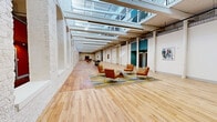 Located at 201 S 12th St in Bessemer City, NC, this expansive single-floor space is a masterfully renovated historic structure that seamlessly blends industrial heritage with modern design sensibilities. The open floor plan stretches the full length of the building, offering a generous and flexible layout ideal for a variety of uses.

Architectural character defines this space at every turn. Whitewashed brick walls with arched openings and painted columns line the interior, preserving the building's original industrial character while providing a bright, clean aesthetic. Soaring ceilings are complemented by a striking skylight system that runs the length of the space, flooding the interior with abundant natural light throughout the day.

The flooring tells its own story, transitioning between richly patinated original hardwood and newer light wood planks, reflecting the building's layered history. Accent walls in deep teal and bold red punctuate the white-dominated palette, adding visual energy and defining different zones within the open layout.

Casual seating arrangements with contemporary lounge chairs and area rugs create inviting gathering areas, while high-top tables and bar-stool seating offer more functional workspace configurations. Exposed ductwork and industrial-style lighting fixtures above reinforce the space's adaptive reuse character. Additional utility features, including a heavy-duty access door, are also present.