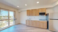 Located at 2701 Shattuck Ave in Berkeley, CA, this efficiently designed single-floor studio offers a bright and functional living space. Light wood-tone luxury vinyl plank flooring runs throughout, lending a clean, contemporary feel to the entire unit.

The open kitchen is outfitted with warm honey-toned wood cabinetry extending from floor to ceiling, offering generous storage. A sleek white countertop houses a single-basin sink, a smooth-top cooktop, an over-the-range microwave, and a full-size refrigerator — providing all essential cooking amenities in a compact, well-organized layout.

The main living area is flooded with natural light through a large set of floor-to-ceiling windows and a sliding glass door that opens to an elevated view of the surrounding Berkeley neighborhood, including tree canopy and distant skyline glimpses. A wall-mounted mini-split HVAC system ensures year-round climate comfort.

The bathroom features light wood cabinetry with a white countertop vanity, a full soaking tub with overhead shower, white tile surround, grab bar, and matching light flooring that ties seamlessly to the rest of the unit. An in-unit stacked washer and dryer adds a practical and convenient amenity. Recessed lighting throughout keeps the space feeling open and well-illuminated.