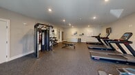 Located at 105 Pomeroy Ave in Meriden, Connecticut, this dedicated fitness center offers a well-appointed exercise space designed to support a full range of workout routines. The room features durable speckled rubber flooring throughout, providing a safe and functional surface for all types of physical activity.

The space is outfitted with a comprehensive selection of equipment, including multiple treadmills, an elliptical machine, and a stationary bike for cardiovascular training. A multi-functional cable machine and a flat weight bench, paired with a tiered dumbbell rack holding a complete set of free weights, cater to strength training needs. A large wall-mounted mirror spans one side of the room, enhancing the sense of openness and allowing users to monitor their form during workouts.

Recessed lighting illuminates the space evenly from above, complementing the natural light that enters through several windows fitted with white blinds. An accent wall in a warm terracotta tone adds a vibrant contrast to the neutral gray walls, lending the room a welcoming energy. A wall-mounted television is positioned for convenient viewing during cardio sessions. A glass-paneled exterior door provides direct outdoor access, further brightening the environment. Decorative artwork and a small storage shelf complete the polished, functional aesthetic of this exercise facility.