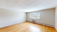 Located at 56 Charlesbank Way in Waltham, MA, this two-bedroom, one-bathroom residence offers a practical and well-organized single-floor layout. Gleaming hardwood floors run throughout the living areas and bedrooms, lending warmth and continuity to the space. The living room is the largest area of the home, featuring a textured ceiling, a wall-mounted AC unit, baseboard heating, and a window with blinds that invites natural light and outdoor views. Both bedrooms continue the hardwood flooring theme and include windows that bring in additional daylight; the primary bedroom offers a comfortable and well-proportioned retreat, while the second bedroom provides flexible space. The kitchen is equipped with warm-toned wood cabinetry, granite-look countertops, a standard range, a dishwasher, and a refrigerator, all set atop neutral tile flooring. A dining nook adjacent to the kitchen features a window overlooking the surrounding neighborhood. The bathroom includes a full tub-shower combination with classic white tile accented by teal trim and a window for natural ventilation. Two hallways provide smooth connectivity between rooms, completing this straightforward and functional home layout.