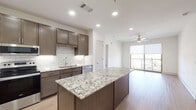 This single-floor residence is designed with a contemporary aesthetic, blending functionality with modern finishes throughout. The open-concept layout connects the kitchen and living area seamlessly, creating a cohesive and spacious feel underscored by light wood-style flooring and recessed lighting.

The kitchen is a standout feature, equipped with dark-toned shaker cabinetry, a classic white subway tile backsplash with under-cabinet lighting, and striking granite countertops featuring bold veining. A generously sized center island provides additional prep and seating space, while stainless steel appliances—including a refrigerator with ice maker, range, microwave, and dishwasher—complete the setup.

The living area benefits from natural light through large sliding glass doors that open to a private balcony with modern metal railing. A ceiling fan adds comfort to this bright, airy space.

The bedrooms feature plush carpeting, ceiling fans, and windows with outdoor views. The bathrooms are finished with matching granite vanity tops, dark wood cabinetry, and tiled shower and tub combinations. Walk-in closets with built-in shelving provide ample storage. Overall, the unit presents a clean, cohesive design with quality finishes throughout.